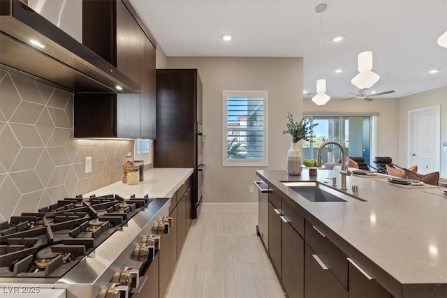 kitchen with sink, wall chimney range hood, appliances with stainless steel finishes, hanging light fixtures, and decorative backsplash