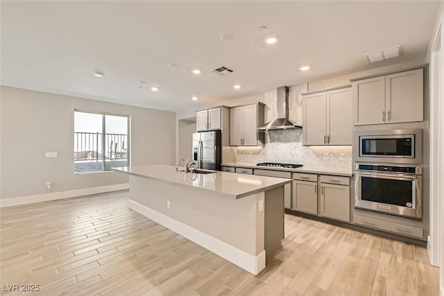 kitchen with appliances with stainless steel finishes, light countertops, wall chimney range hood, and gray cabinetry