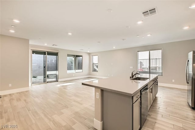 kitchen with visible vents, open floor plan, a kitchen island with sink, stainless steel appliances, and a sink