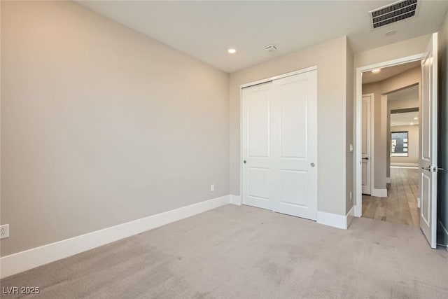 unfurnished bedroom with baseboards, visible vents, a closet, and light colored carpet