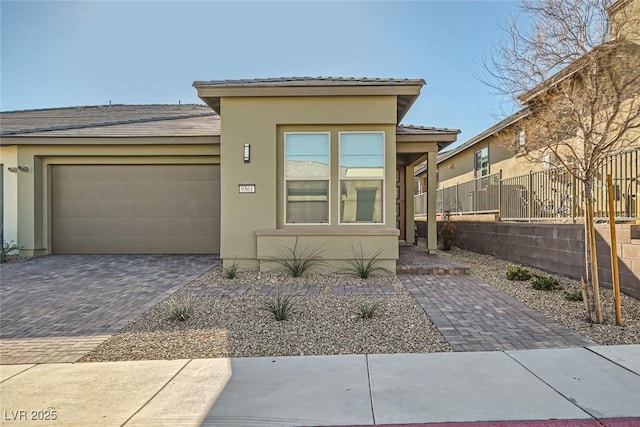 prairie-style house featuring a garage, decorative driveway, fence, and stucco siding