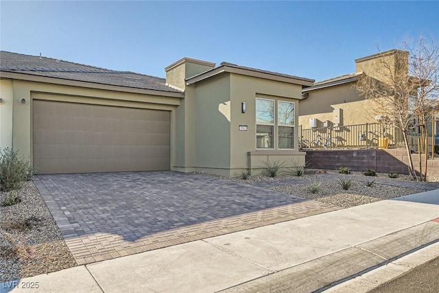 view of front of house featuring decorative driveway, an attached garage, and stucco siding