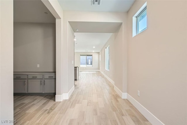 hall with visible vents, light wood-style flooring, and baseboards