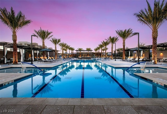 pool at dusk with a patio area and a community pool