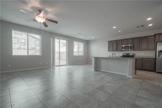 kitchen featuring sink, light tile patterned floors, a kitchen island with sink, stainless steel appliances, and light stone countertops