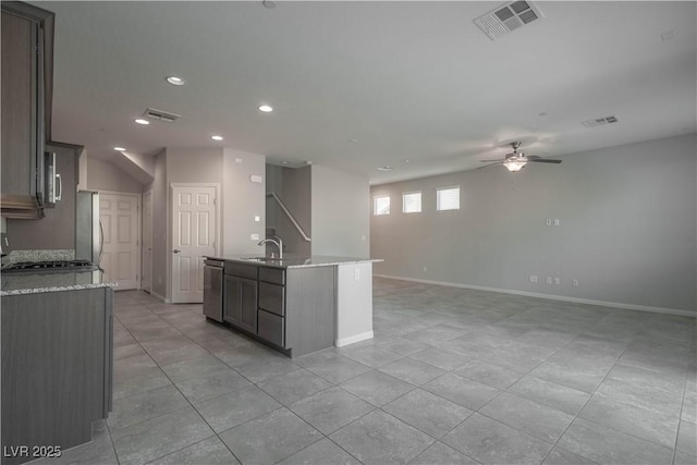 kitchen with sink, ceiling fan, appliances with stainless steel finishes, light stone counters, and an island with sink