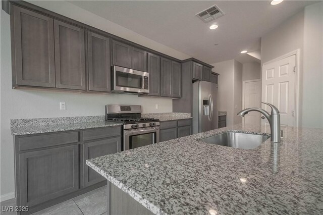 kitchen featuring light stone counters, appliances with stainless steel finishes, sink, and light tile patterned floors