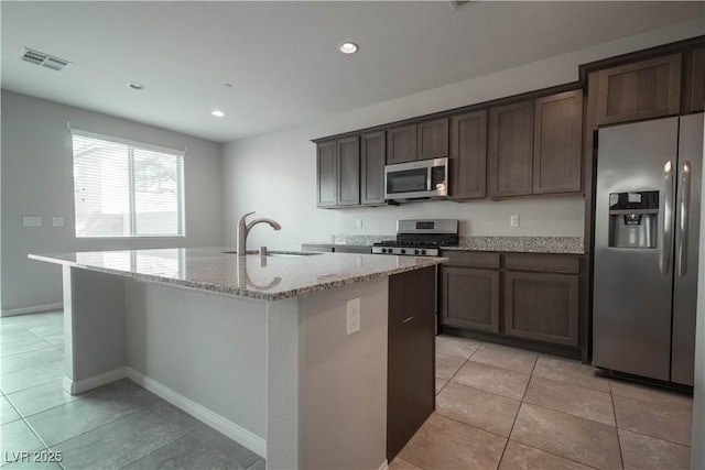 kitchen featuring sink, light tile patterned floors, stainless steel appliances, light stone countertops, and an island with sink