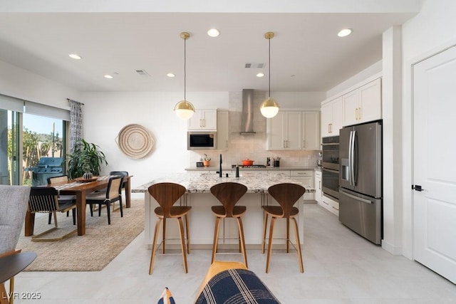 kitchen with a breakfast bar area, stainless steel appliances, tasteful backsplash, white cabinetry, and wall chimney range hood