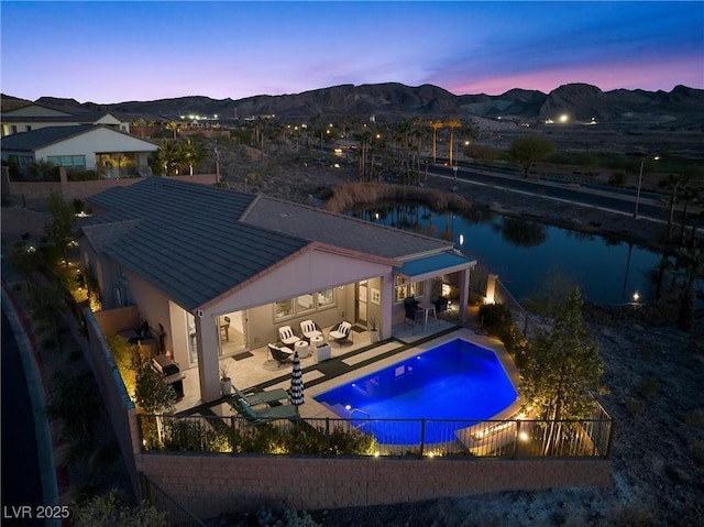 pool at dusk with exterior kitchen, an outdoor living space, a mountain view, and a patio