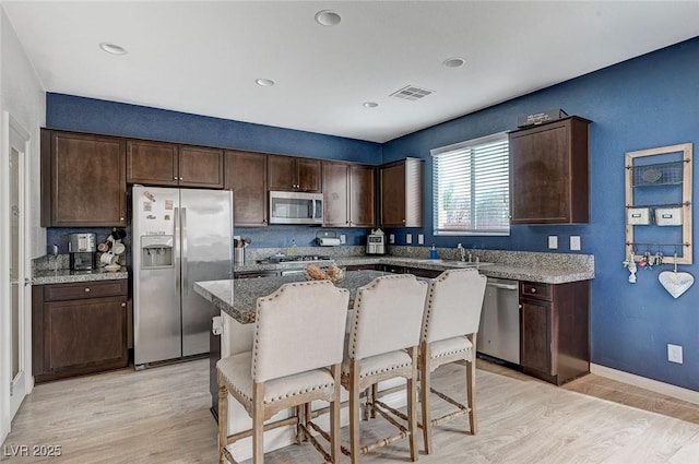 kitchen with dark brown cabinetry, appliances with stainless steel finishes, a center island, and light stone countertops