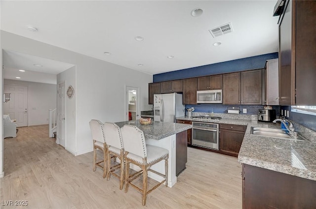 kitchen featuring sink, light hardwood / wood-style flooring, appliances with stainless steel finishes, a center island, and light stone countertops