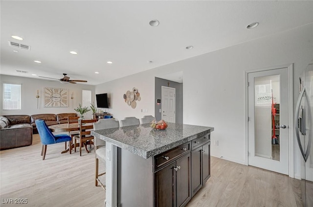 kitchen with light hardwood / wood-style flooring, a kitchen breakfast bar, a center island, dark brown cabinetry, and stone countertops