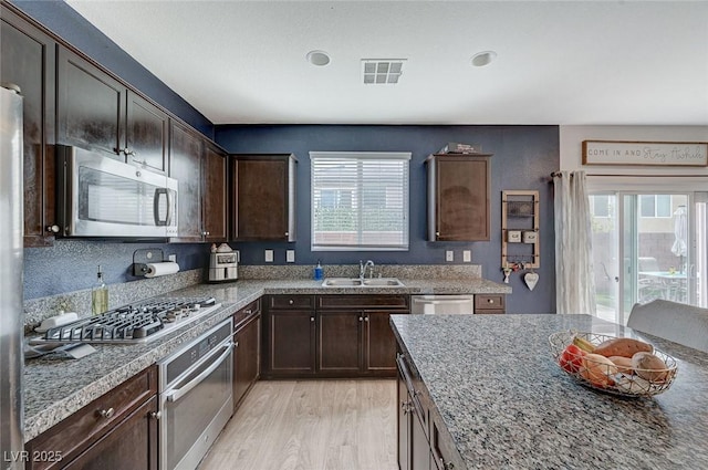 kitchen featuring sink, stone counters, appliances with stainless steel finishes, dark brown cabinets, and light wood-type flooring