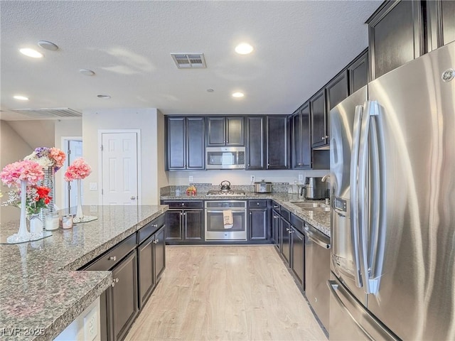 kitchen featuring appliances with stainless steel finishes, light wood-type flooring, a textured ceiling, and dark stone counters