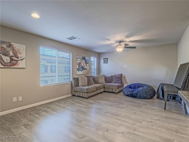 living room featuring ceiling fan, light hardwood / wood-style floors, and a textured ceiling