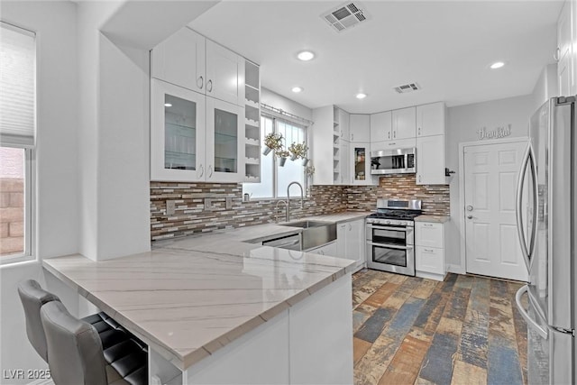 kitchen with light stone counters, kitchen peninsula, white cabinets, and appliances with stainless steel finishes