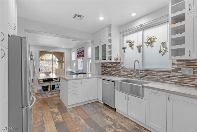 kitchen with sink, appliances with stainless steel finishes, kitchen peninsula, white cabinets, and backsplash