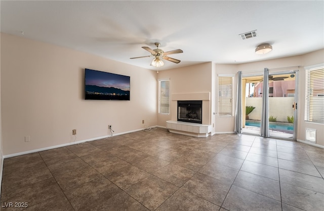 unfurnished living room featuring a tiled fireplace, dark tile patterned flooring, and ceiling fan