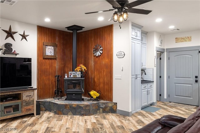 living room featuring sink, light hardwood / wood-style flooring, ceiling fan, and a wood stove