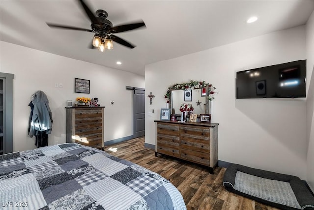 bedroom with ceiling fan, a barn door, and dark hardwood / wood-style flooring