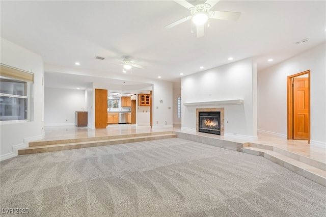 unfurnished living room featuring light carpet, a tile fireplace, and ceiling fan