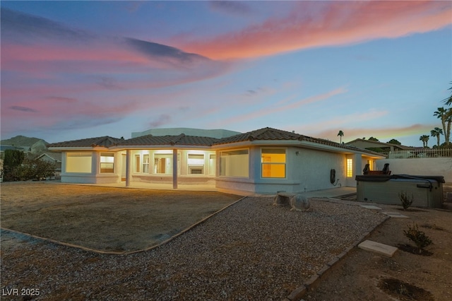 back house at dusk featuring a hot tub and a patio area