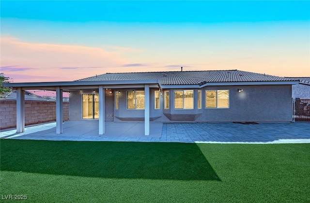 back house at dusk with a patio area and a lawn