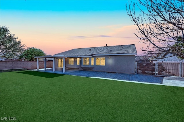 back house at dusk featuring a patio and a yard