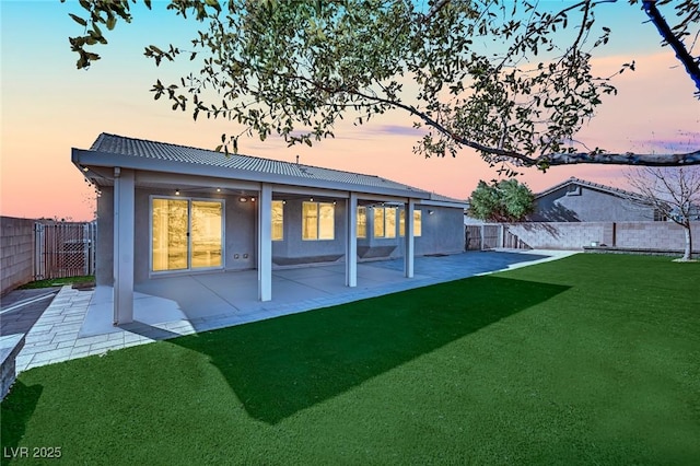 back house at dusk with a patio and a lawn