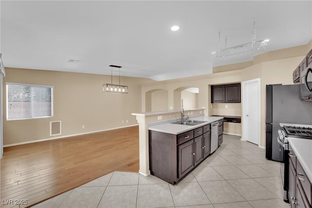 kitchen with sink, hanging light fixtures, dark brown cabinetry, stainless steel gas range, and light hardwood / wood-style flooring