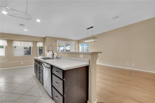 kitchen with dark brown cabinetry, sink, decorative light fixtures, a center island with sink, and stainless steel dishwasher