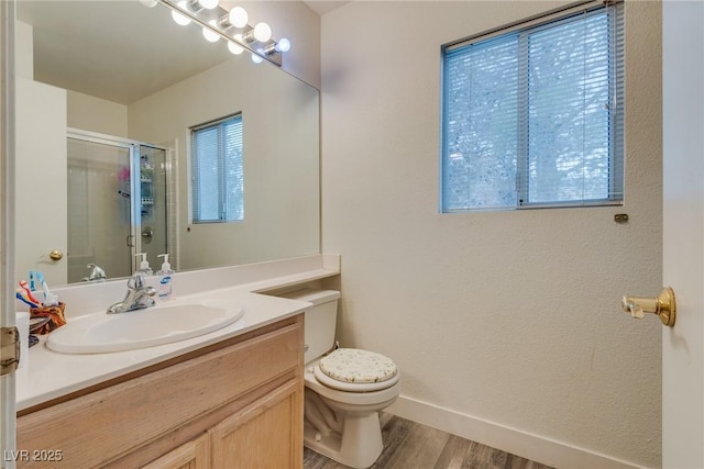 bathroom featuring toilet, a shower with shower door, wood-type flooring, vanity, and plenty of natural light