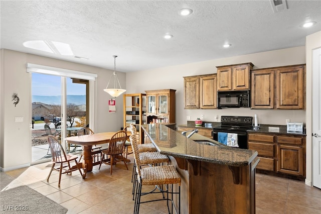 kitchen featuring sink, a breakfast bar, dark stone countertops, hanging light fixtures, and black appliances