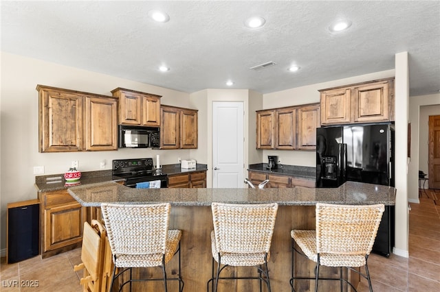 kitchen with dark stone countertops, a breakfast bar area, black appliances, and a kitchen island