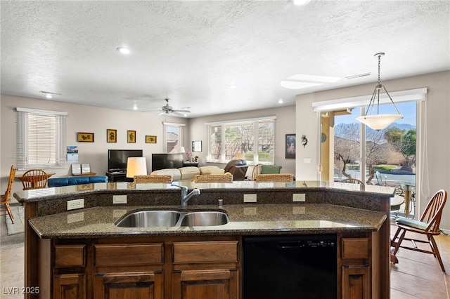 kitchen with light tile patterned flooring, sink, dishwasher, an island with sink, and dark stone counters