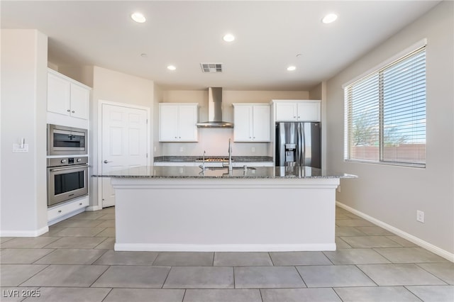 kitchen with stainless steel appliances, an island with sink, white cabinetry, and wall chimney exhaust hood