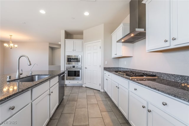 kitchen with appliances with stainless steel finishes, sink, white cabinets, dark stone counters, and wall chimney range hood