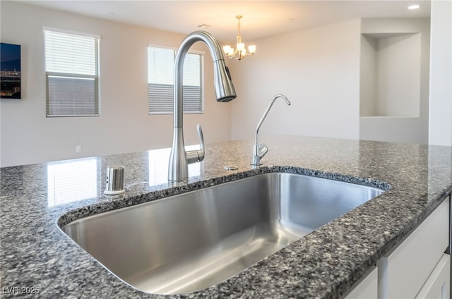 details with sink, white cabinetry, decorative light fixtures, a chandelier, and dark stone countertops