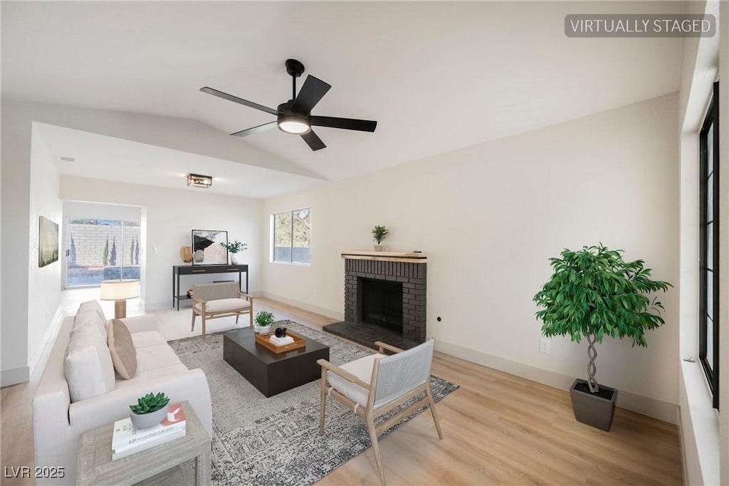 living room featuring light hardwood / wood-style flooring, a brick fireplace, vaulted ceiling, and ceiling fan