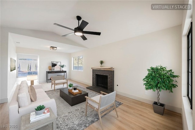 living room featuring light hardwood / wood-style flooring, a brick fireplace, vaulted ceiling, and ceiling fan