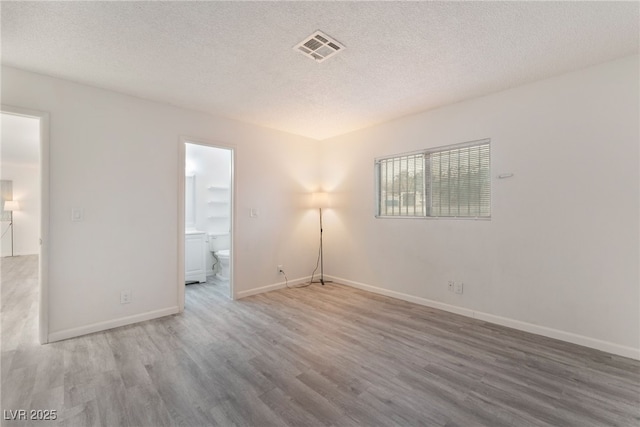 empty room with baseboards, a textured ceiling, visible vents, and wood finished floors