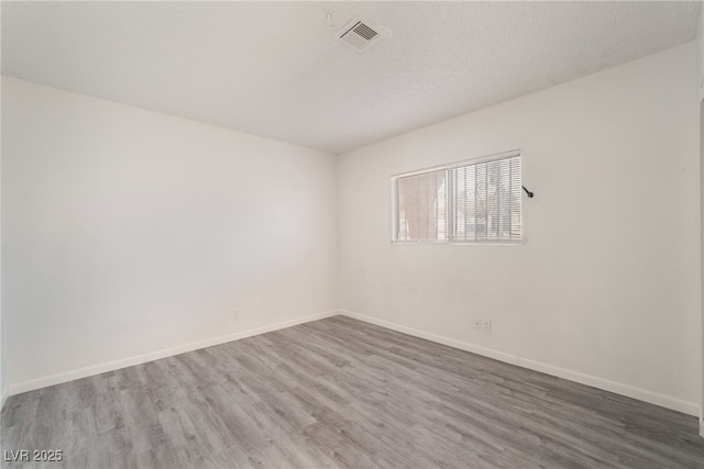 unfurnished room with baseboards, a textured ceiling, visible vents, and wood finished floors