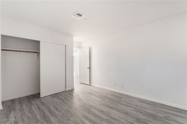 unfurnished bedroom featuring baseboards, visible vents, wood finished floors, a textured ceiling, and a closet