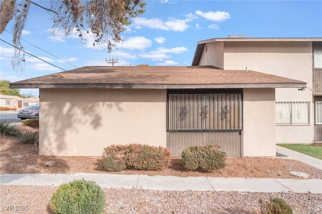 view of side of property featuring a shingled roof and stucco siding