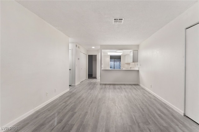 unfurnished living room with visible vents, light wood-style flooring, baseboards, and a textured ceiling