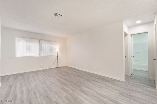 unfurnished room with light wood finished floors, baseboards, visible vents, and a textured ceiling