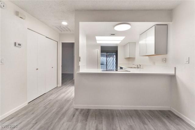 kitchen with a peninsula, visible vents, white cabinets, light countertops, and light wood-type flooring