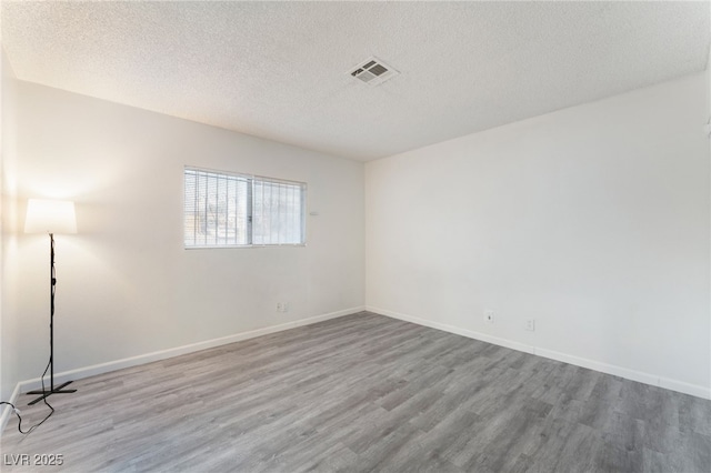 unfurnished room featuring baseboards, a textured ceiling, visible vents, and wood finished floors