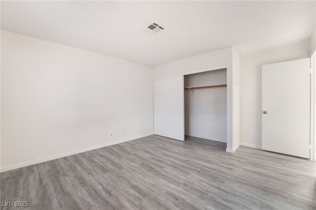 unfurnished bedroom featuring a closet, visible vents, a textured ceiling, wood finished floors, and baseboards